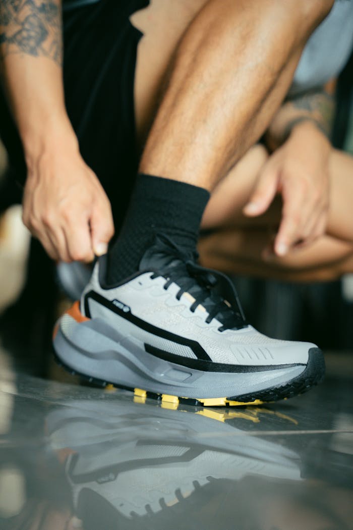 about-01 Close-up of a man tying a modern athletic shoe on a reflective surface indoors.